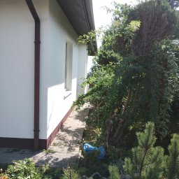 Euro styl wykończenia wnętrz Stanisław Moskwa - Biała elewacja domu jednorodzinnego w Strzyżowie z brązowymi akcentami, widoczna z poziomu ogrodu. Ścieżka z kostki prowadzi wzdłuż ściany.