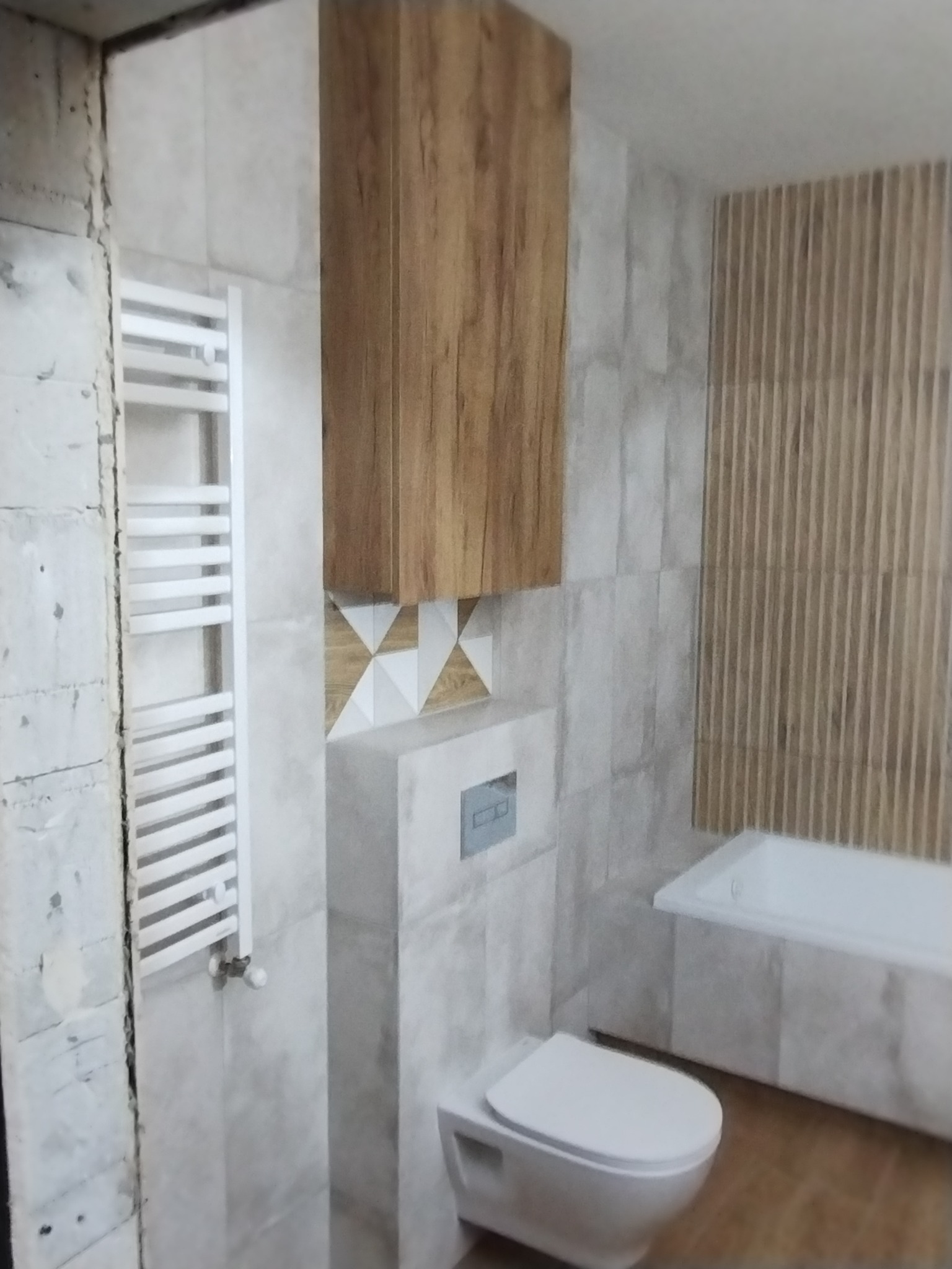 Wykończona łazienka z wiszącą szafką z drewnianym frontem, grzejnikiem drabinkowym, toaletą i wanną, ściany wyłożone płytkami imitującymi kamień oraz dekoracyjnymi lamelami.