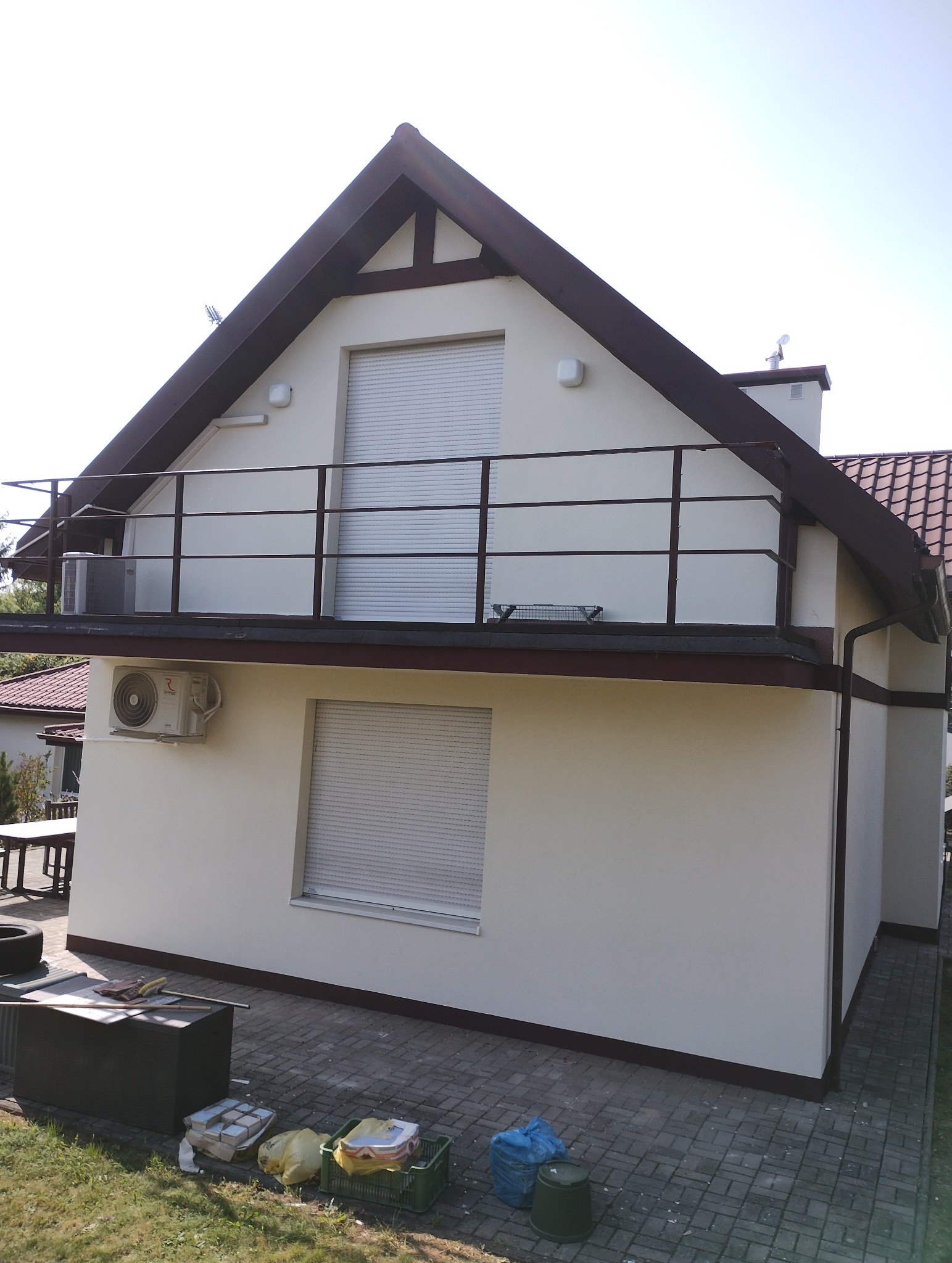 Odnowiona elewacja domu z balkonem i brązowymi elementami wykończeniowymi. Widoczne narzędzia i materiały malarskie sugerują świeżo zakończone prace.