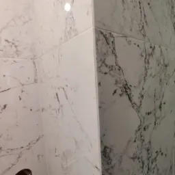 Ściana narożna wyłożona białymi płytkami imitującymi marmur w łazience w Chwaszczynie, widoczne precyzyjne fugi.