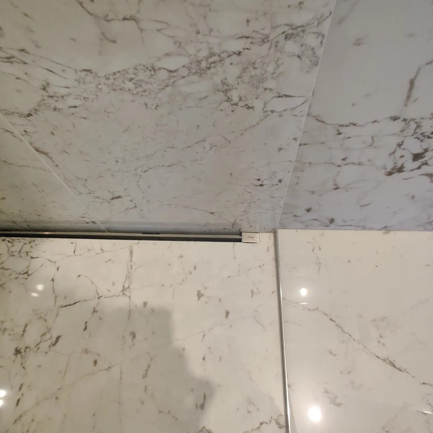 Ułożone płytki imitujące marmur, z widoczną czarną listwą i małą białą etykietą Viega.