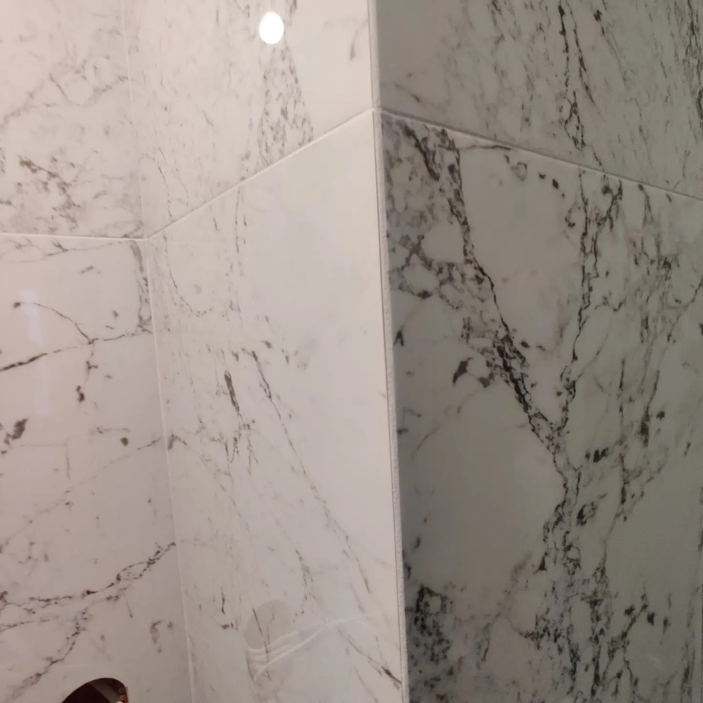 Ściana narożna wyłożona białymi płytkami imitującymi marmur w łazience w Chwaszczynie, widoczne precyzyjne fugi.