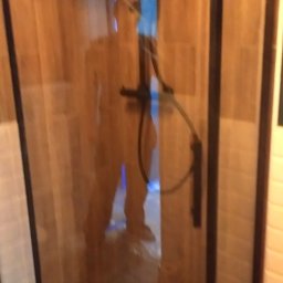 Damian Drankowski - Kabina prysznicowa z czarnymi profilami i drewnianą ścianą w tle, widoczne elementy instalacji wodnej i osoba wewnątrz.