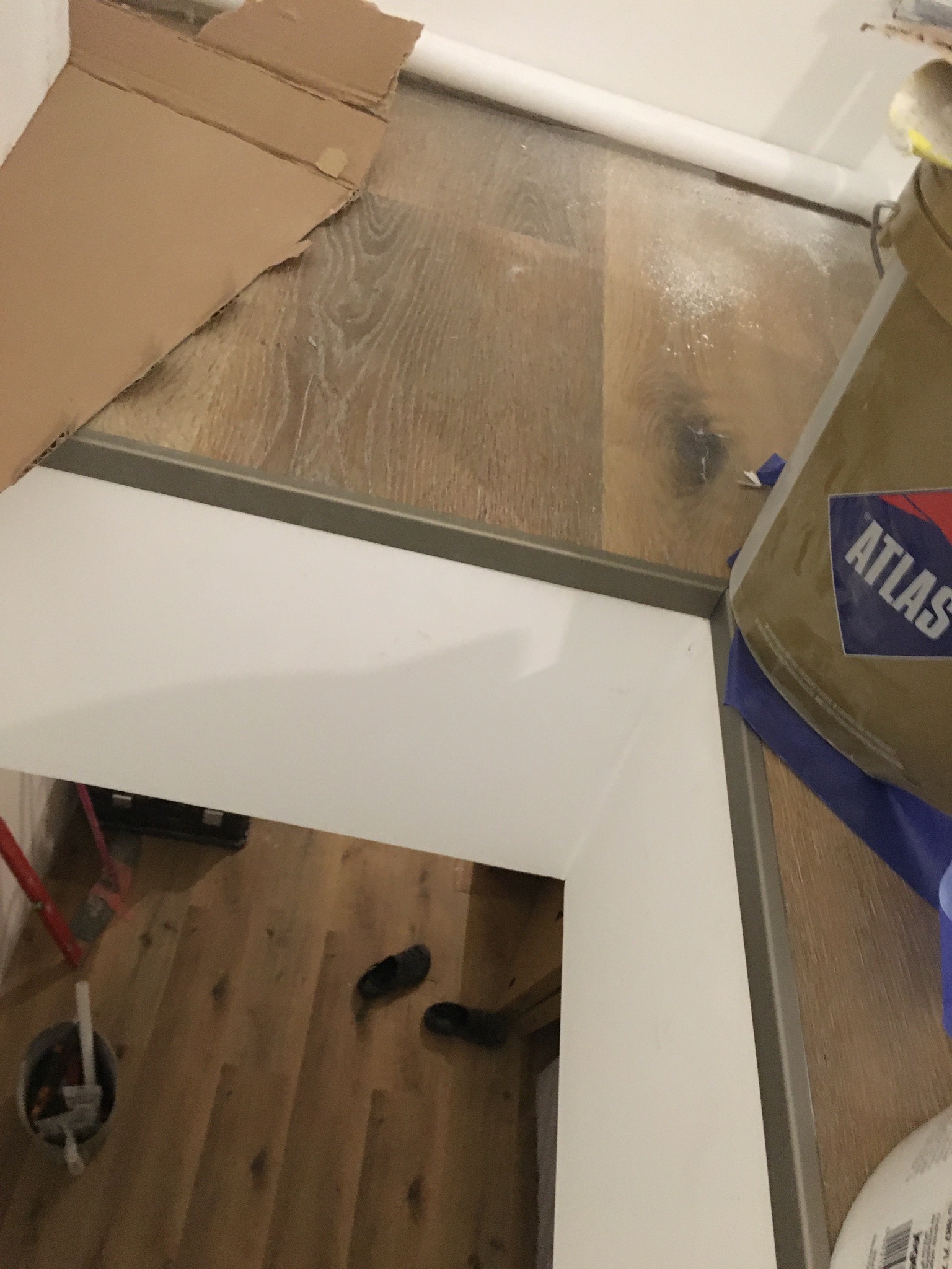 Zabezpieczone podłoże kartonem, wiadro z zaprawą Atlas i narzędzia w tle, widok z góry na przygotowania do prac wykończeniowych.