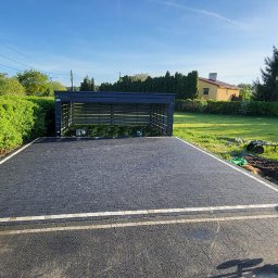 Usługi Brukarsko-Ziemne Oleh Berezovskyi - Nowo ułożona, czarna kostka brukowa z jasnymi obrzeżami na podjeździe. W tle widoczny garaż, zieleń i dom. Na pierwszym planie zagęszczarka.