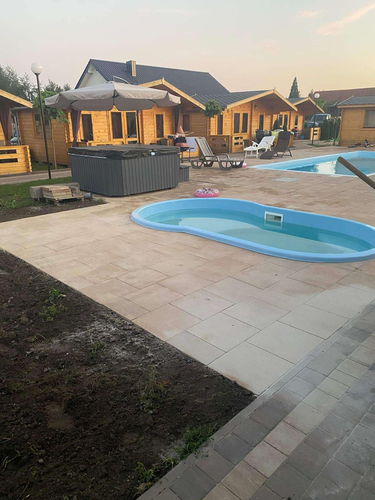 Ułożona kostka brukowa wokół basenu i jacuzzi przy drewnianych domkach letniskowych, widok z poziomu gruntu.