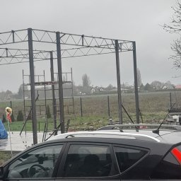 Spaw-Bud Jarosław Komorowski - Stalowa konstrukcja z drabinkami w tle, widoczna przez szybę zaparkowanego, czarnego samochodu w pochmurny dzień.