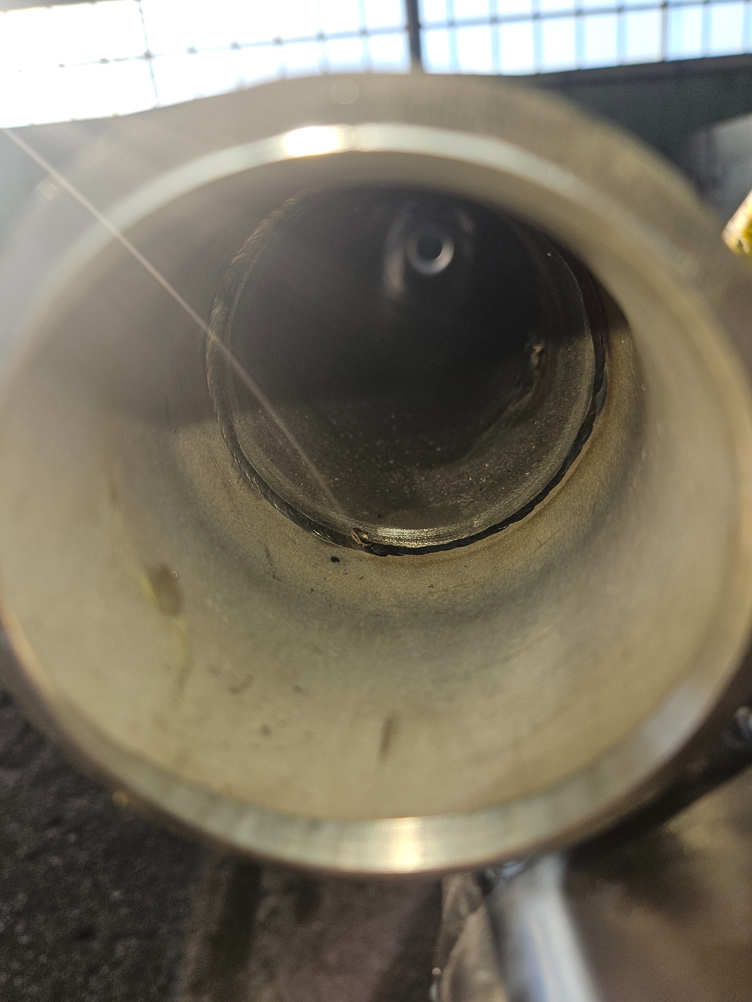 Wewnętrzny widok rury ze stali nierdzewnej ze świeżym spoiwem spawalniczym, widoczne ślady obróbki i niedoskonałości spoiny, oświetlone światłem dziennym z góry.