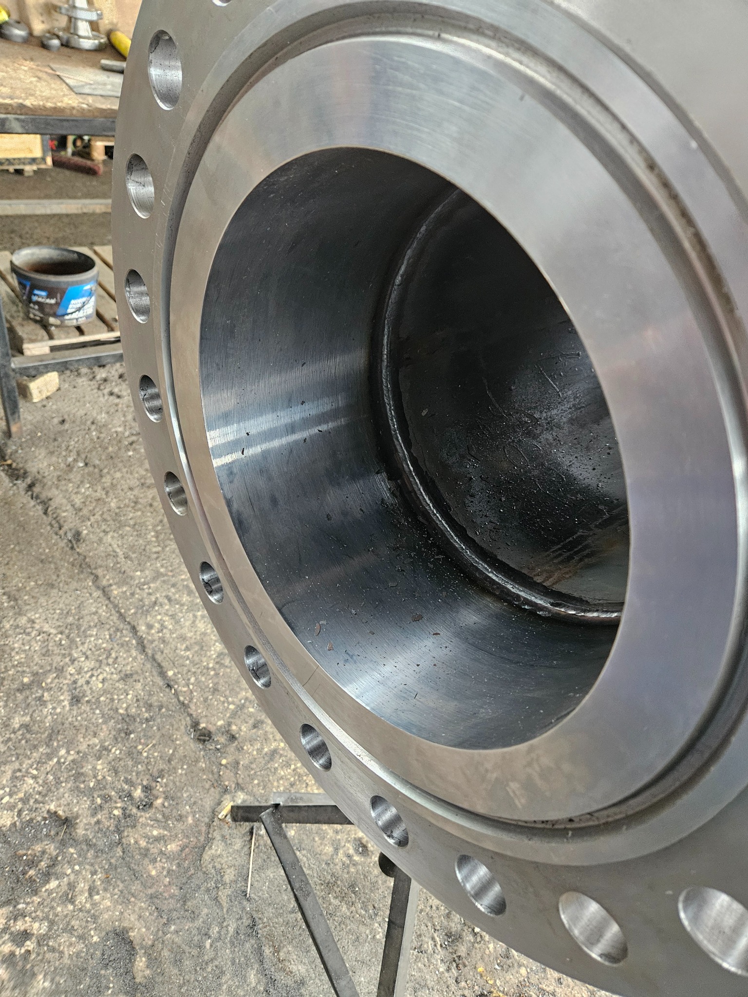 Szczegółowe ujęcie spawanej, stalowej rury kołnierzowej z widocznym spawem wewnętrznym i otworami na śruby, umieszczonej na metalowym stojaku.