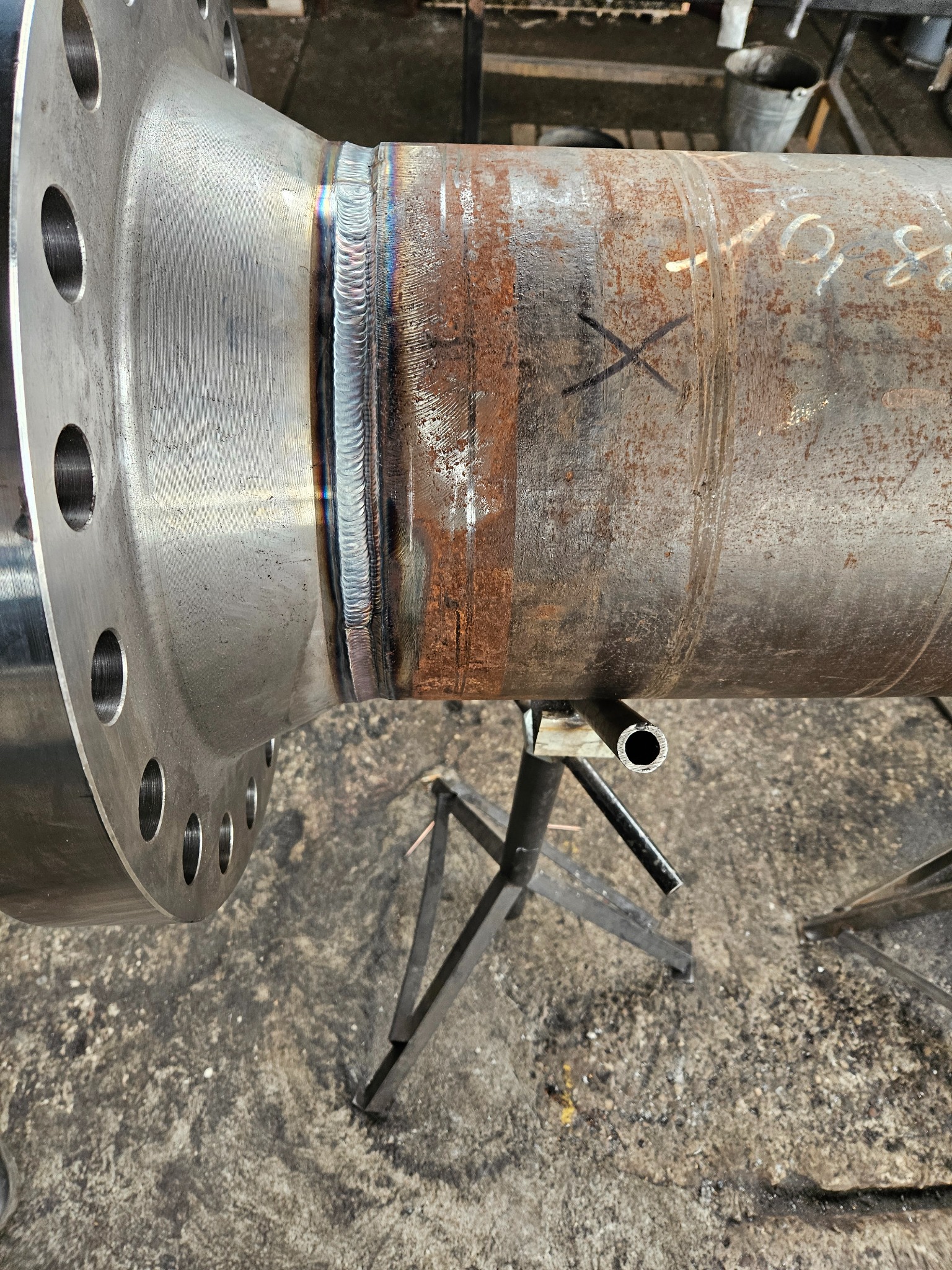 Spoina łącząca rdzewiejącą rurę z kołnierzem, umieszczona na metalowym stojaku.