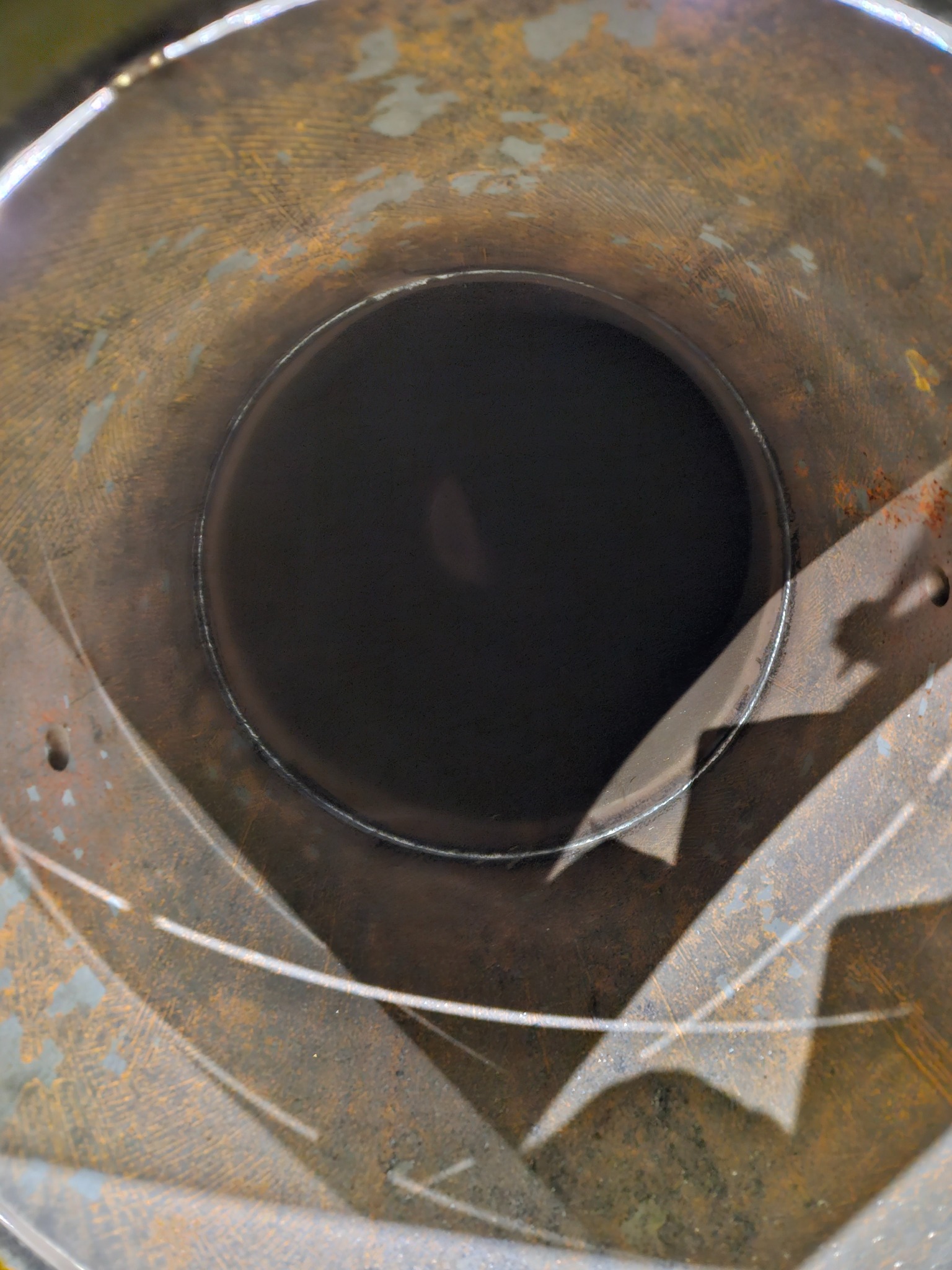 Wnętrze rury metalowej z widocznym spoinem, pokrytej rdzą i śladami użytkowania, oświetlone z góry.