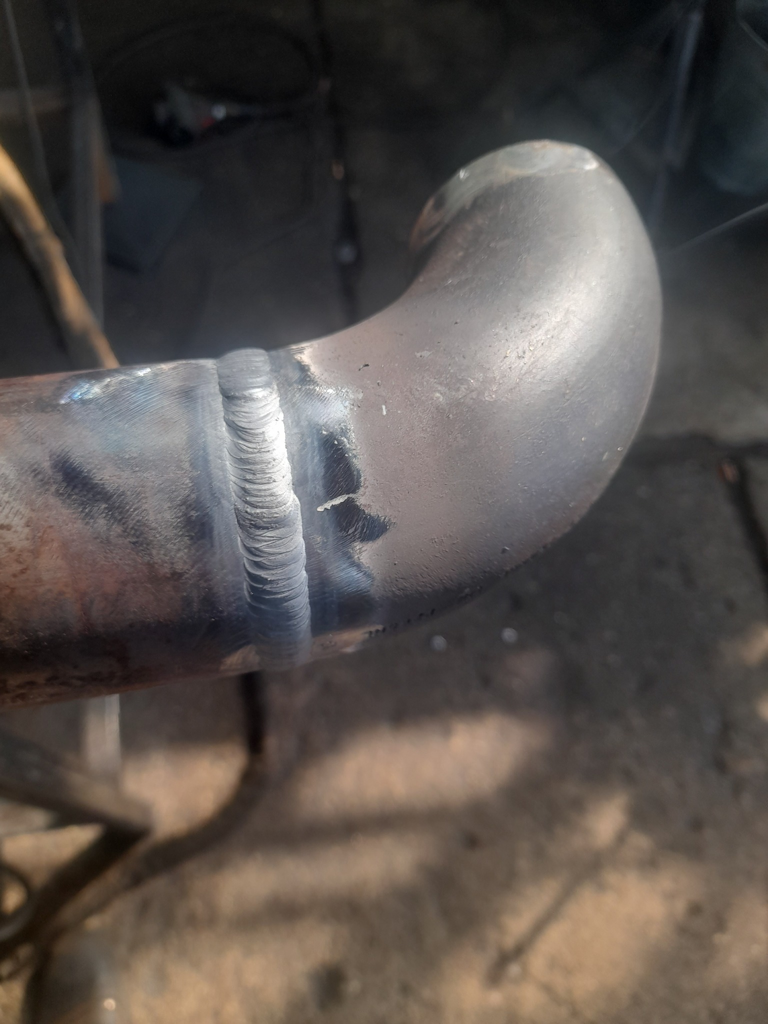 Spoina łącząca dwa metalowe elementy rurowe pod kątem, widoczne ślady obróbki i zmatowienia metalu.