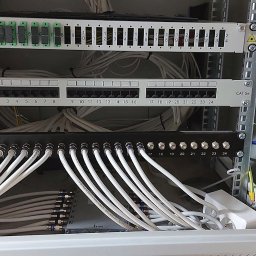 TechnoFix - Szafa rackowa z panelami światłowodowym, krosowym RJ45 Cat 5e i koncentrycznym, z podłączonymi białymi kablami sygnałowymi i przewodem uziemiającym.