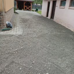 TRAW-KOP Tomasz Musiał - Ukończona ścieżka z szarego żwiru, prowadząca od kostki brukowej obok budynku do drewnianej altany w tle. Widoczny worek i miotła.