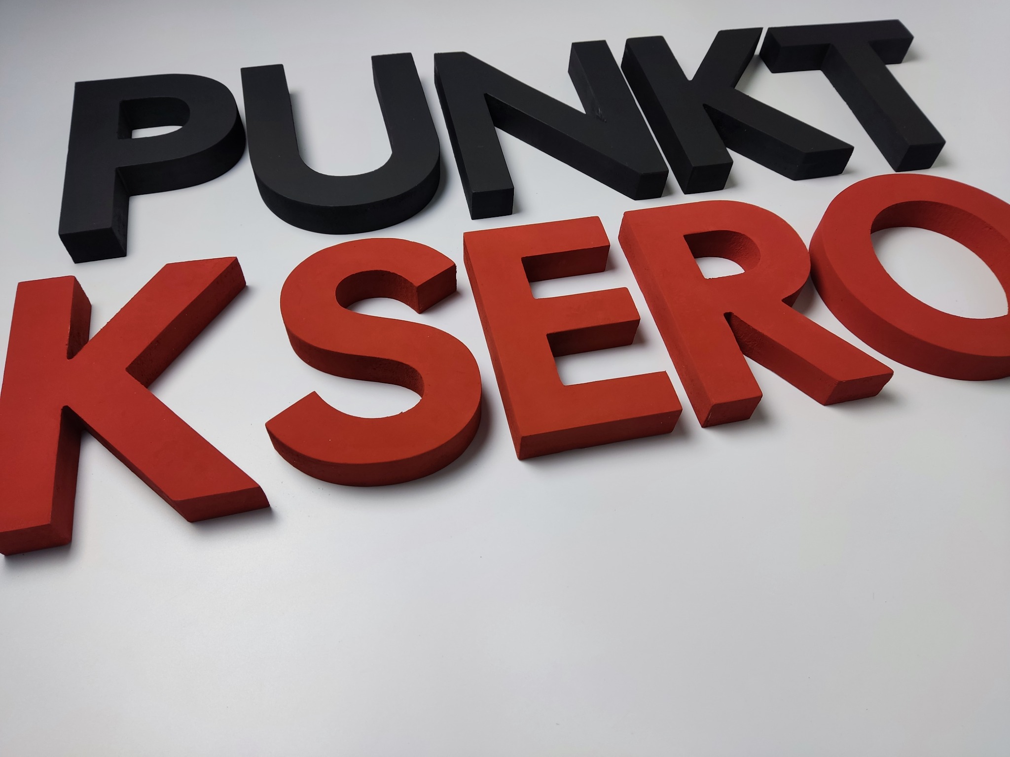 Czerwone i czarne przestrzenne litery układające się w napis 'PUNKT KSERO' na białym tle, widok z góry pod kątem.