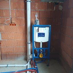 MSJ Instal Marcin Jurkowski - Instalacja podtynkowa WC Villeroy&Boch w surowym wnętrzu. Widoczne rury doprowadzające wodę (czerwone i niebieskie) oraz odpływ. Ściany z czerwonej cegły.