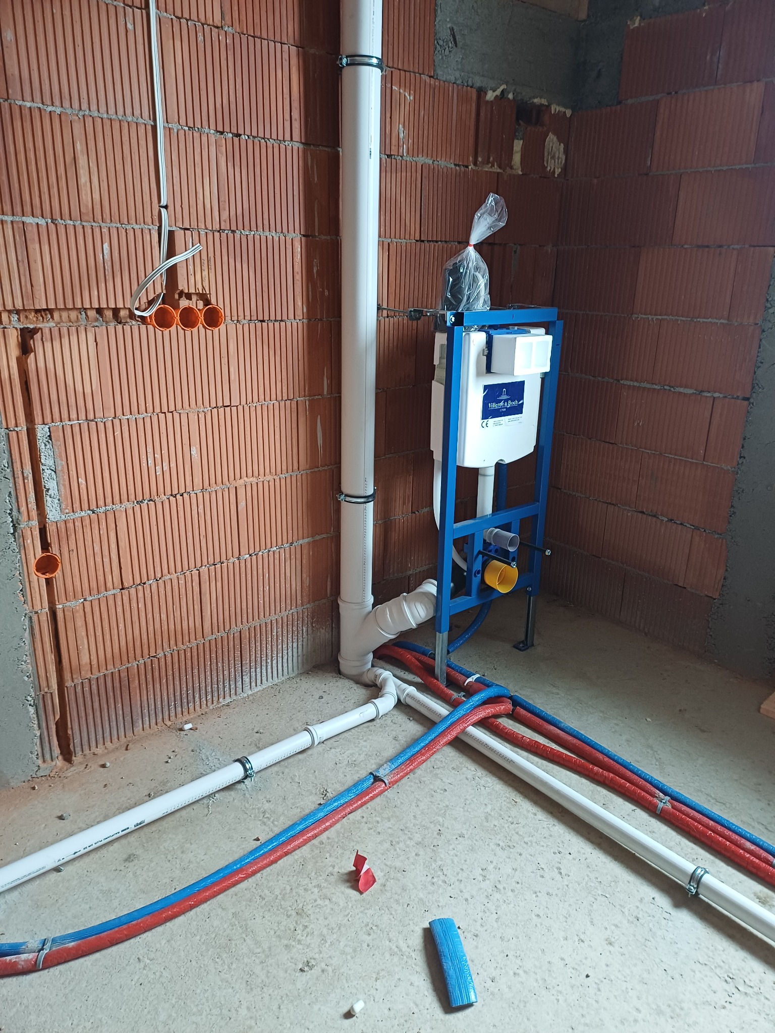 Montaż stelaża podtynkowego WC z instalacją wod-kan w surowym wnętrzu, widok z dołu. Prace hydrauliczne w Frydman.