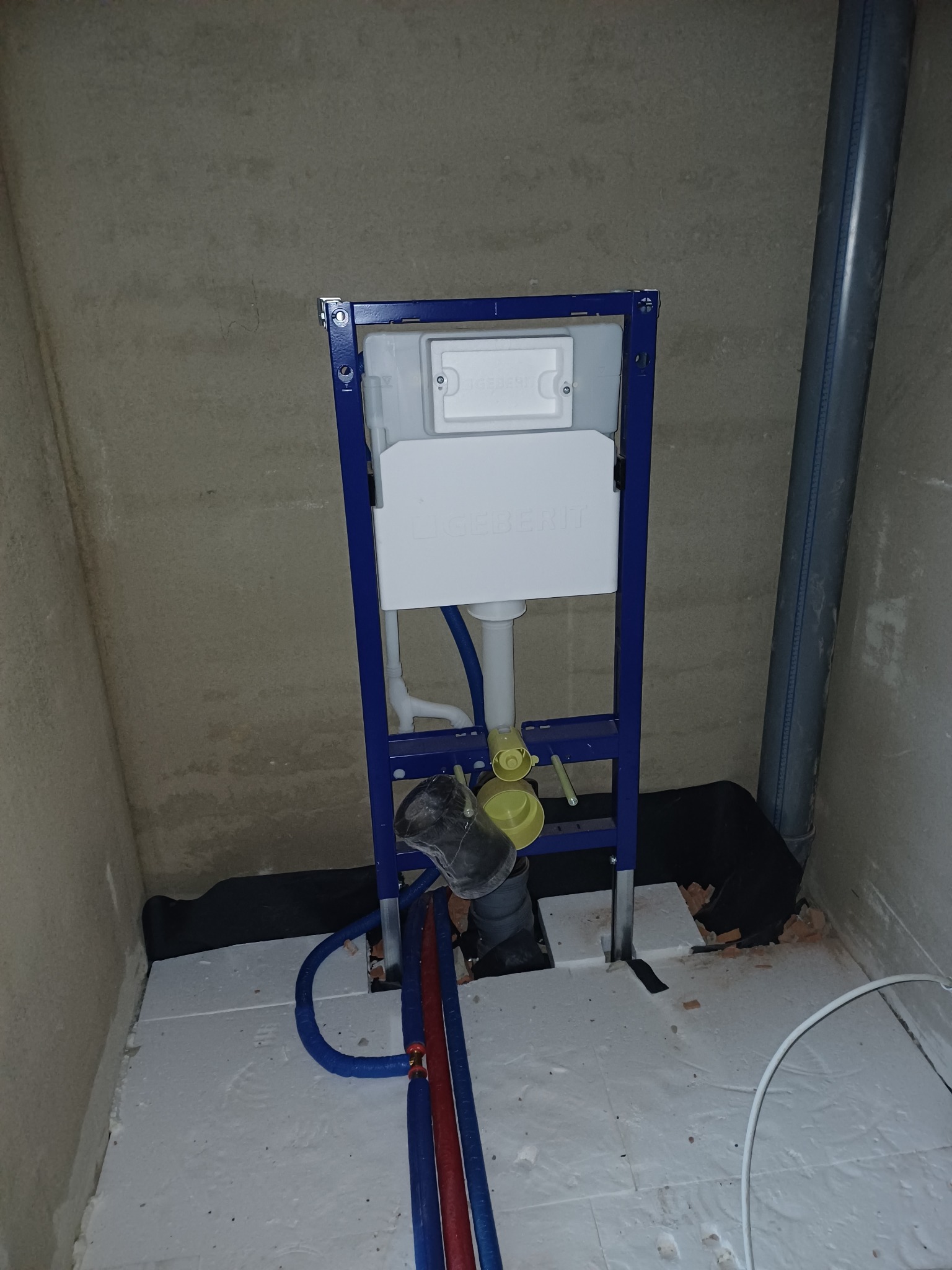 Stelaż podtynkowy Geberit Duofix z widocznymi rurami doprowadzającymi wodę i odpływowymi, zamontowany na podłodze z izolacją, przy surowej ścianie.