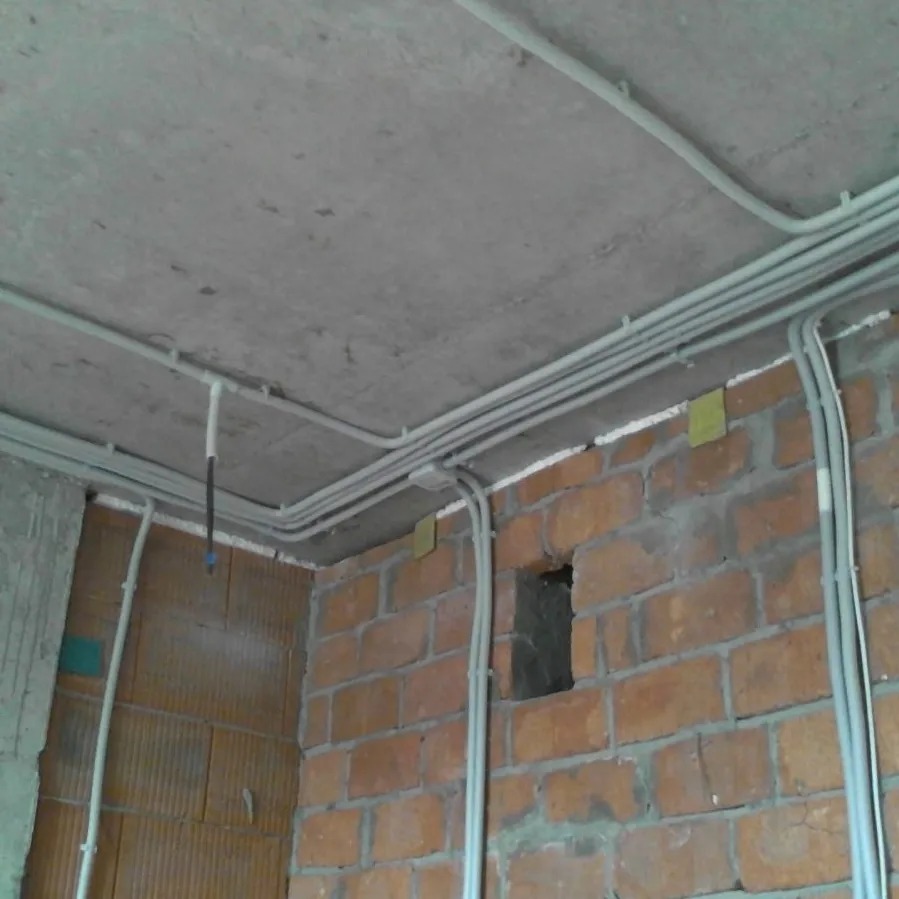 Szare rurki instalacji elektrycznej prowadzone po ceglanej ścianie i betonowym suficie w surowym stanie.