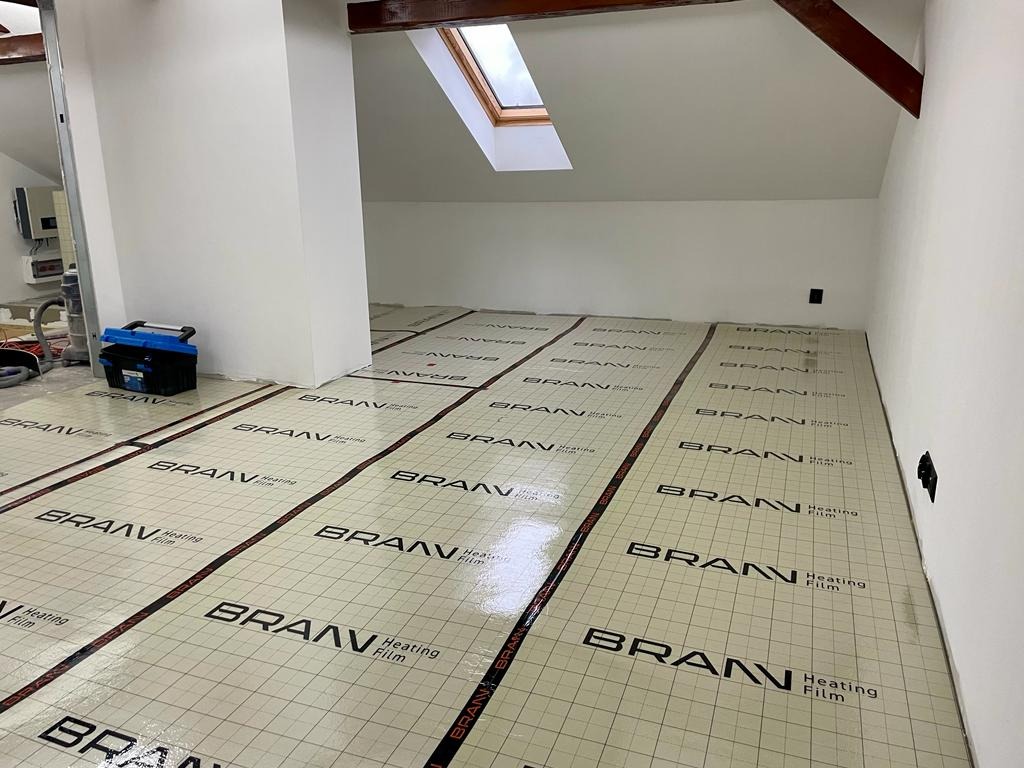Podłoga poddasza pokryta folią grzewczą BRANN Heating Film, widoczne okno dachowe i narzędzia w tle.