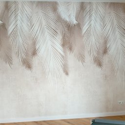 Home serwis-Kafelkowanie - Ściana z beżową tapetą w motywy białych i beżowych liści palmowych, widoczny fragment drewnianej podłogi i listwa przypodłogowa.