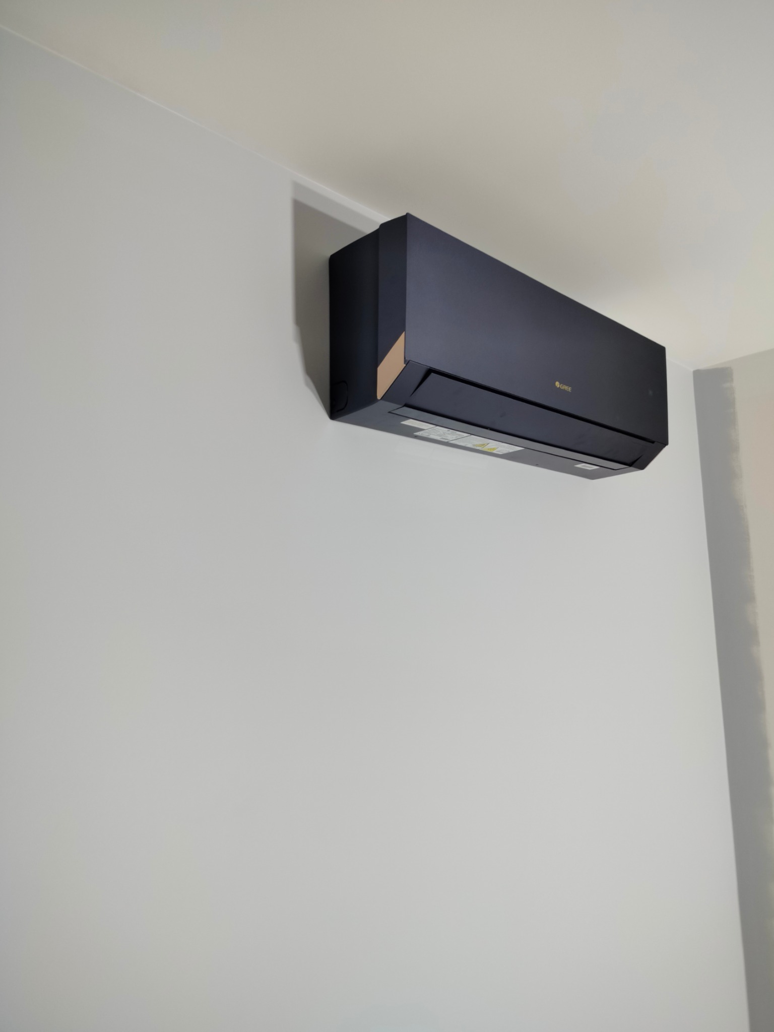 Czarny klimatyzator marki Gree zamontowany na białej ścianie w pomieszczeniu o jasnym oświetleniu.