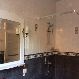 minare.pl - Wykończona łazienka z białymi i ciemnymi marmurkowymi płytkami, lustro z kinkietami i kabina prysznicowa z chromowaną armaturą.