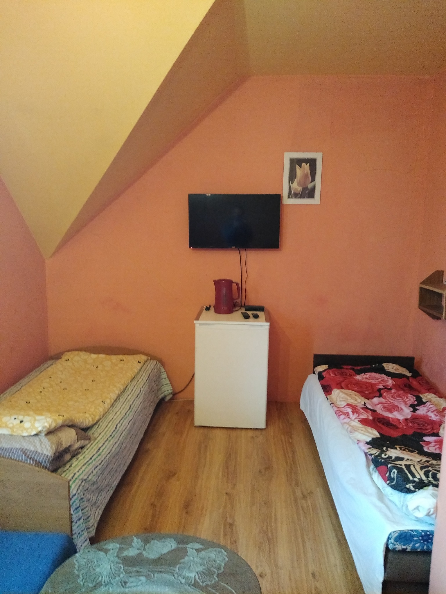 Pokój dwuosobowy na poddaszu z dwoma pojedynczymi łóżkami, małą lodówką, telewizorem i czajnikiem elektrycznym.