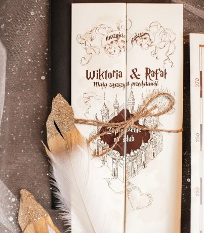 Eleganckie zaproszenie ślubne w stylu vintage z motywem zamku, przewiązane sznurkiem jutowym, ozdobione piórem z brokatem, na tle z delikatnej tkaniny.