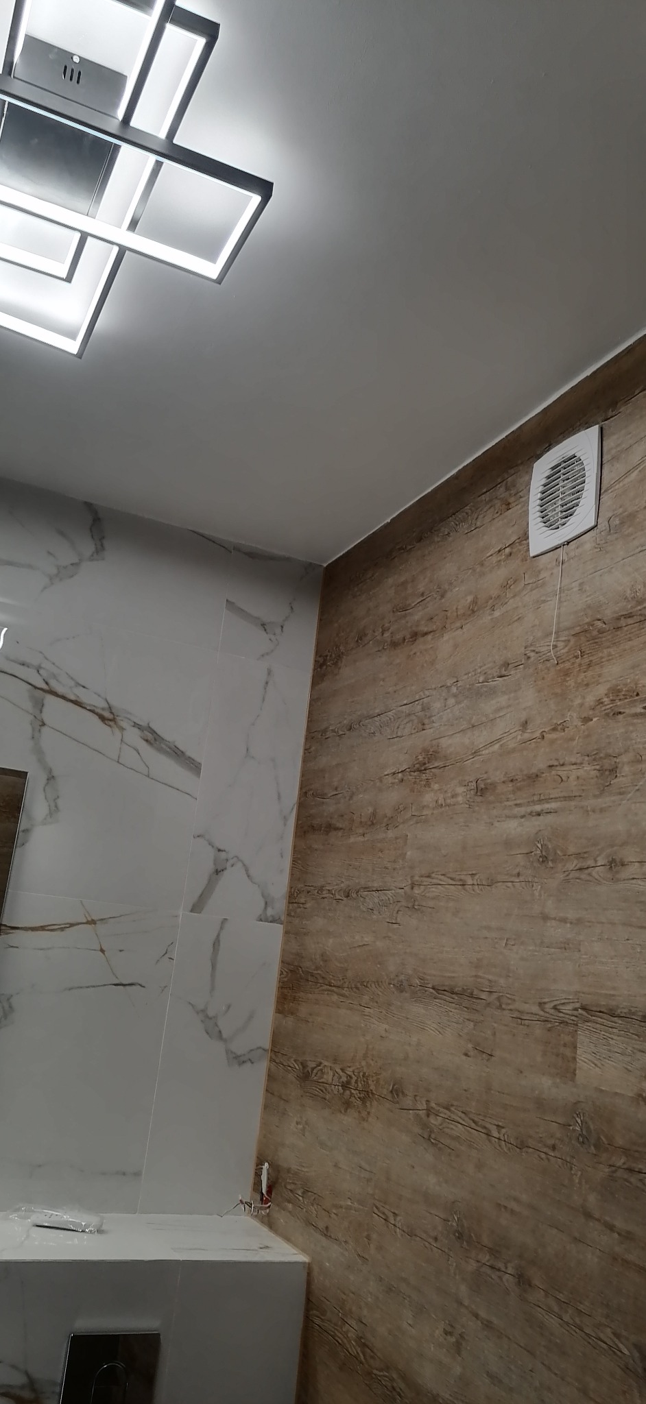 Nowoczesna łazienka z marmurowymi płytkami i drewnopodobną okładziną ścienną, oświetlenie sufitowe LED i wentylator wyciągowy