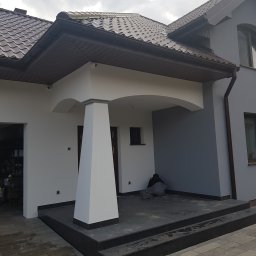 MIX-BUD - Dom jednorodzinny po odświeżeniu elewacji, z widocznym fragmentem tarasu, gdzie pracownik w roboczym ubraniu siedzi na ziemi, prawdopodobnie w trakcie sprzątania po pracach.