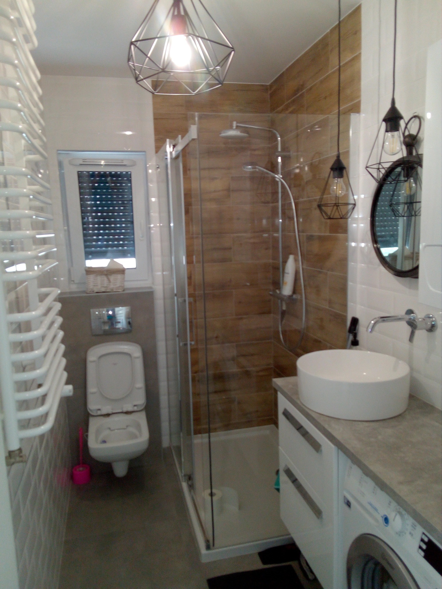 Nowoczesna łazienka z kabiną prysznicową z drewnopodobnymi płytkami, umywalką nablatową, wiszącą toaletą, grzejnikiem drabinkowym i lampami w stylu industrialnym