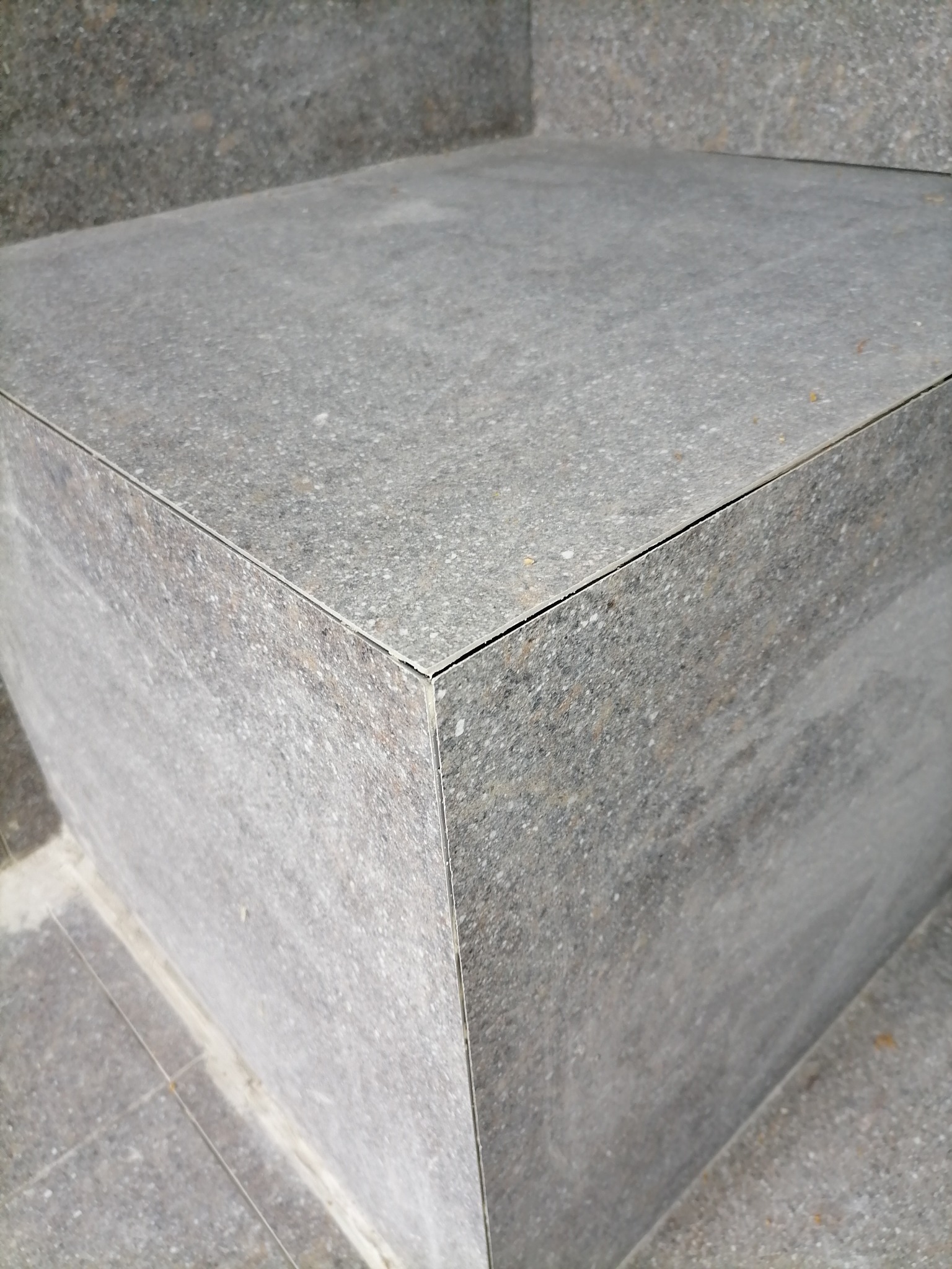 Szary stopień schodów wyłożony płytkami z widocznymi fugami.