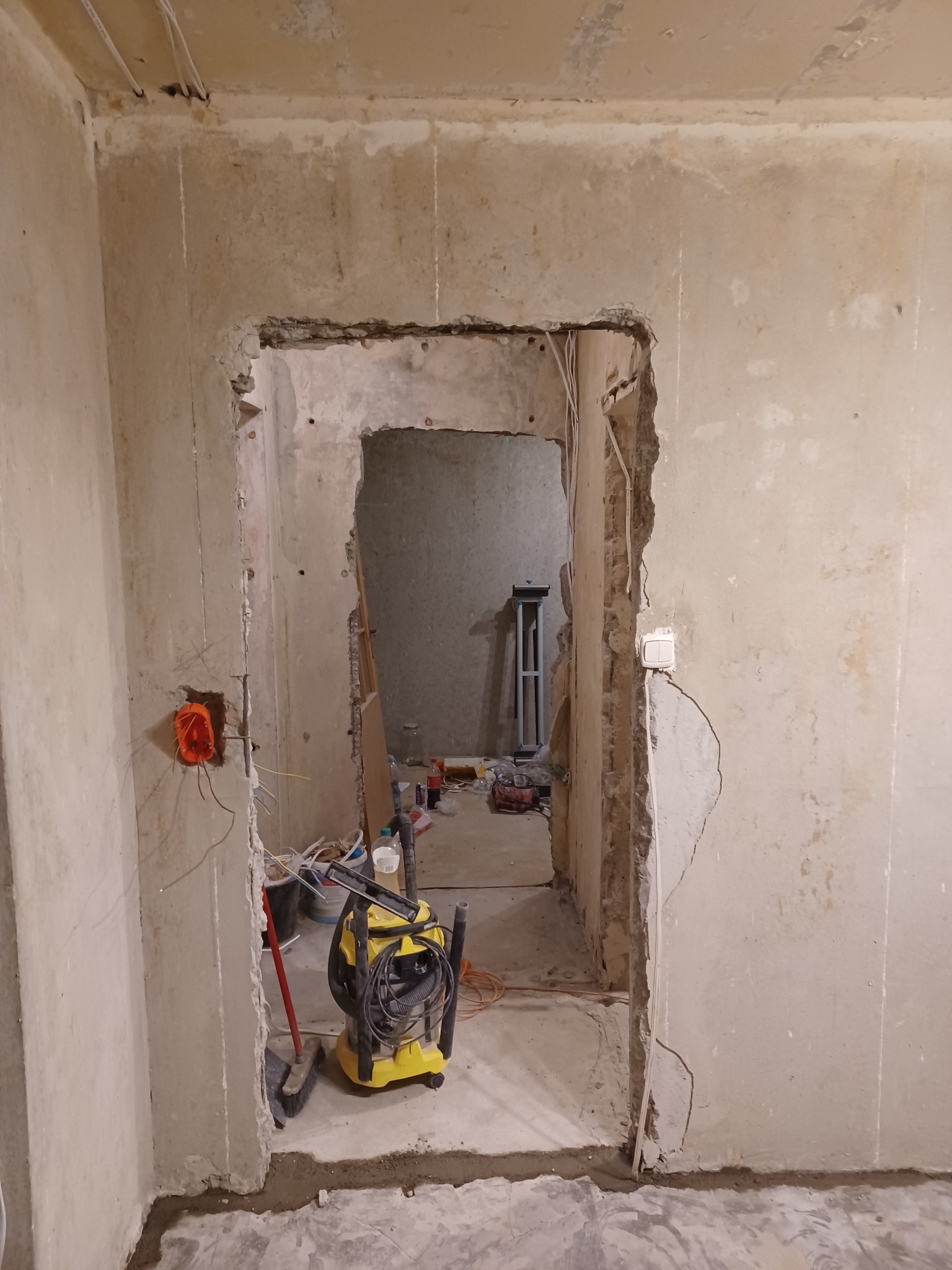 Przygotowanie otworu drzwiowego w surowej ścianie, widoczne przewody elektryczne, puszka instalacyjna oraz żółty odkurzacz przemysłowy.