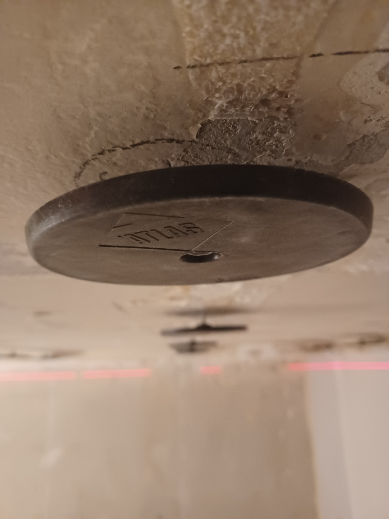 Szlifowanie sufitu gipsowego za pomocą szlifierki z okrągłą tarczą, widoczne ślady ołówka i nierówności powierzchni.