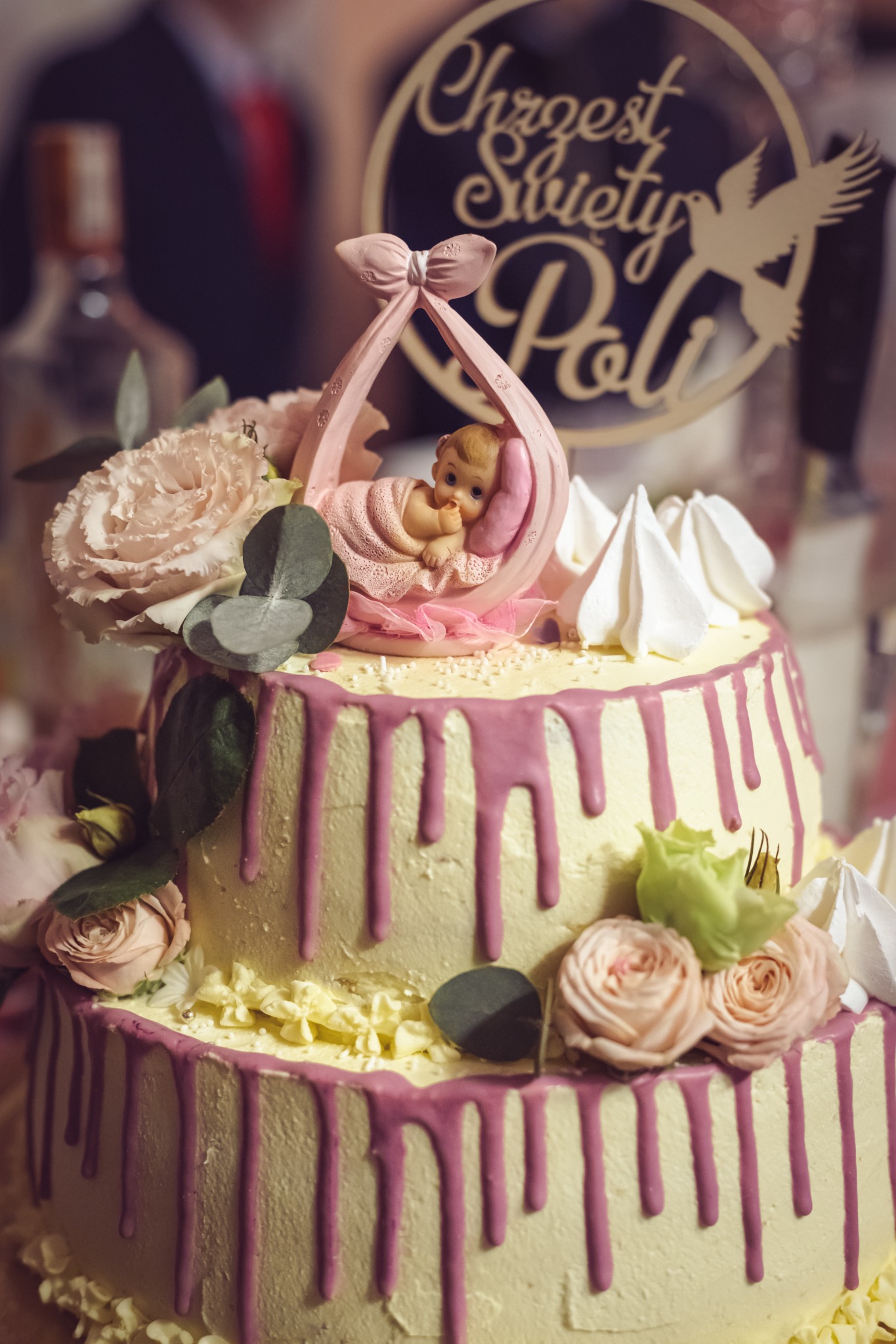 Dwupiętrowy tort z kremem, różowymi polewami i dekoracjami z róż oraz figurką dziecka w kołysce, topper 'Chrzest Święty Poli' z gołębiem.