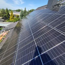 Panel słoneczny na dachu domu w słoneczny dzień, widoczny cień osoby oraz rusztowanie.