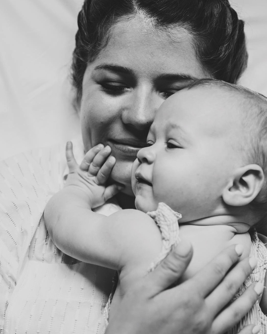 Czarno-białe ujęcie matki trzymającej na rękach małe dziecko, z delikatnym uśmiechem i skupionym wzrokiem dziecka w bok.