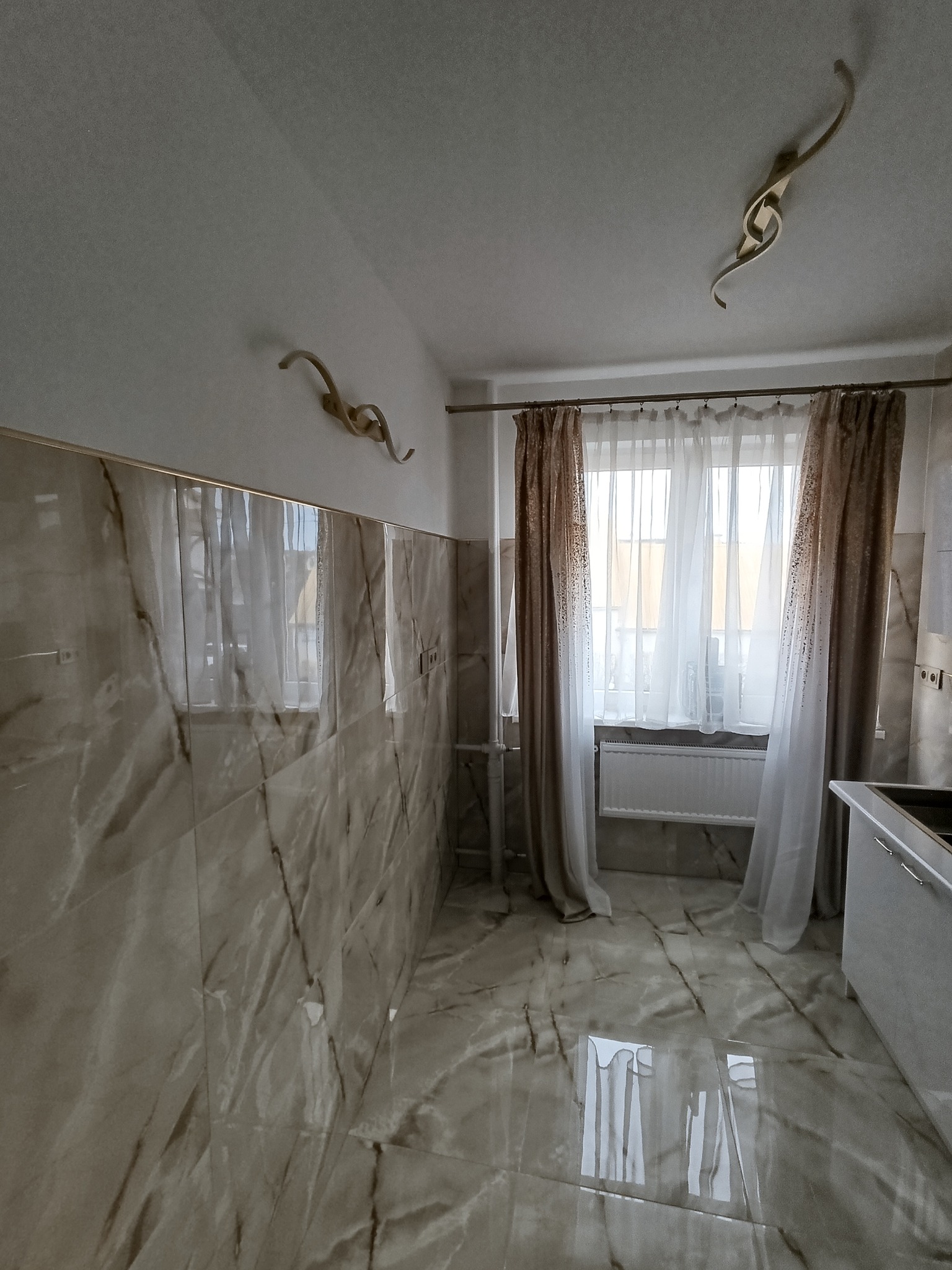 Wykończona kuchnia z marmurowymi płytkami na ścianach i podłodze, dekoracyjnymi lampami na ścianach i zasłonami w oknie.