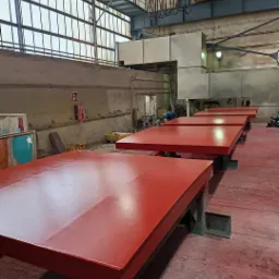 Czerwone, pomalowane na wysoki połysk, stalowe płyty, ustawione w rzędzie w hali produkcyjnej pod suwnicą.