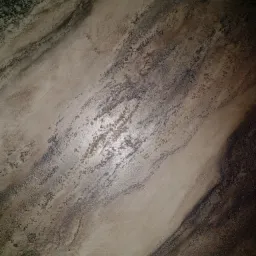 Beżowa ściana z dekoracyjną fakturą imitującą marmur, z ciemnymi żyłkami i delikatnym połyskiem, oświetlona z góry.