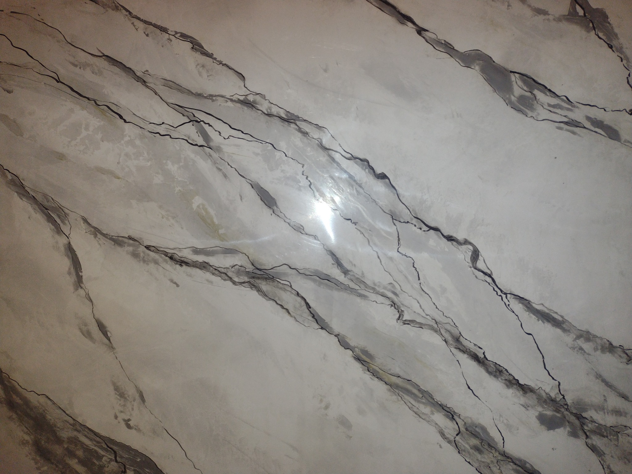 Ściana wykończona szpachlą dekoracyjną imitującą marmur z wyraźnymi, ciemnymi żyłami i błyszczącą powierzchnią.