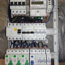 usługi elektryczne ELEKTROWOLF - Rozdzielnica elektryczna z zainstalowanymi bezpiecznikami Eaton, Gacia i licznikiem Orno, widoczne przewody elektryczne, montaż w skrzynce na ścianie pokrytej folią