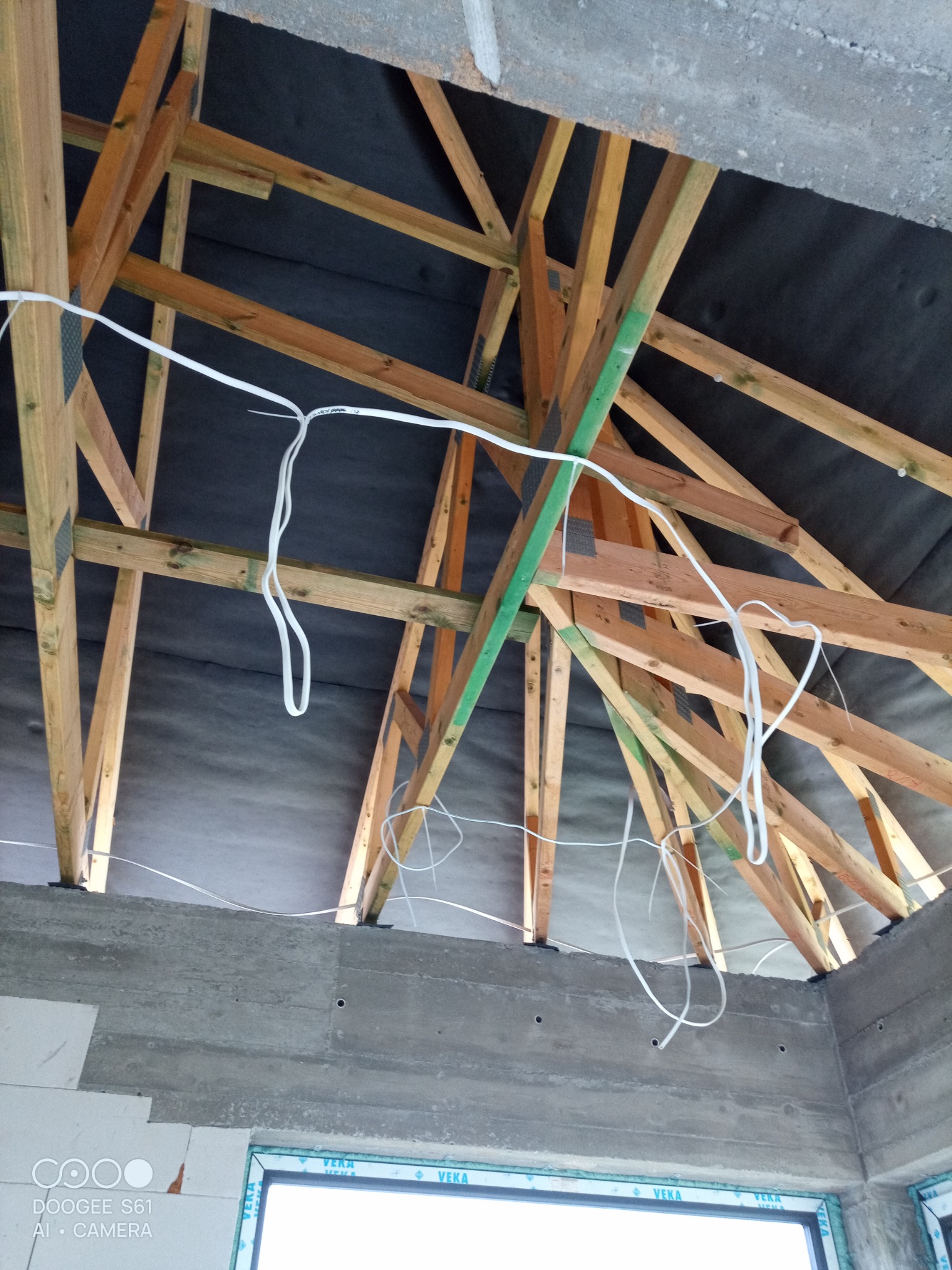 Wiązka białych przewodów elektrycznych zwisająca z drewnianej konstrukcji dachu, widok z wnętrza budynku w trakcie budowy w Wodzisławiu Śląskim.