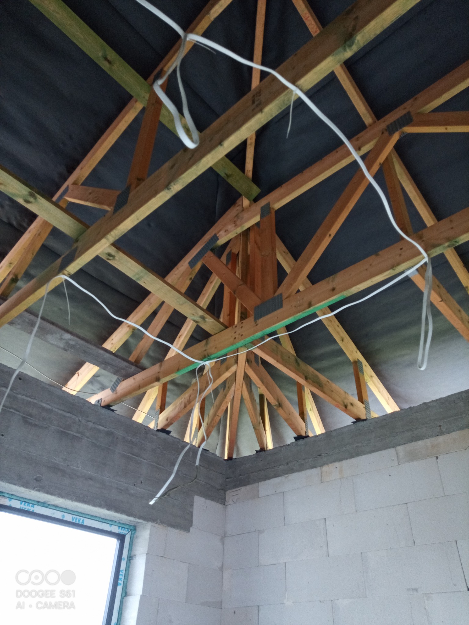 Konstrukcja drewniana dachu z widocznymi kablami elektrycznymi, ujęcie z wnętrza budynku w trakcie budowy.