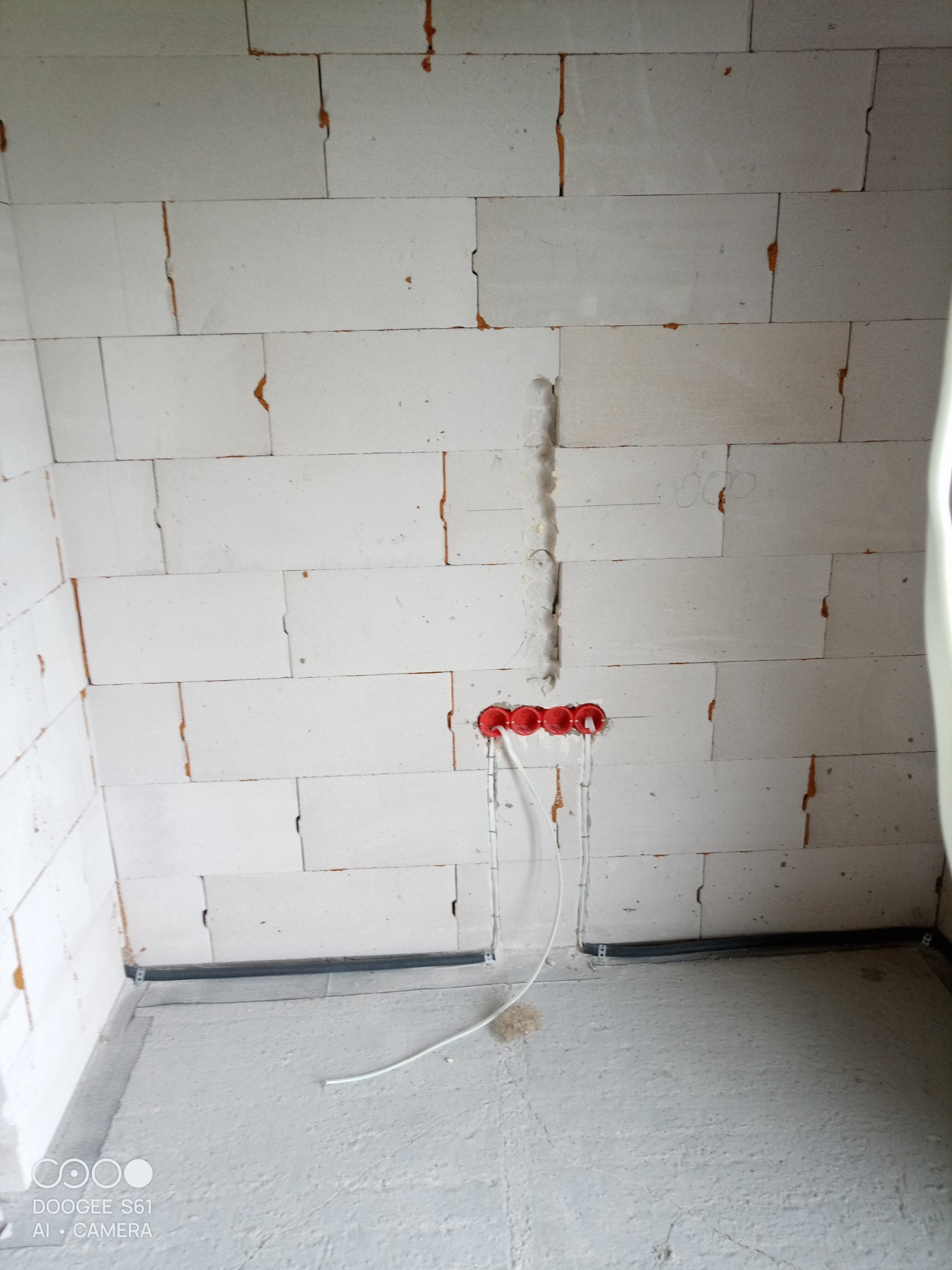 Ściana z betonu komórkowego z wyżłobieniem i zamontowanymi czerwonymi puszkami elektrycznymi, z których wychodzą białe przewody.