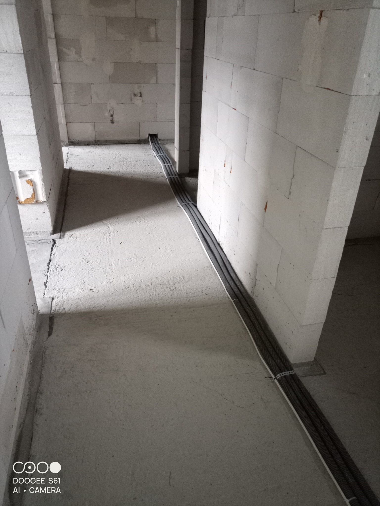 Kable elektryczne w peszlach ułożone na podłodze w surowym wnętrzu budynku z bloczków betonowych, zabezpieczone opaskami zaciskowymi.