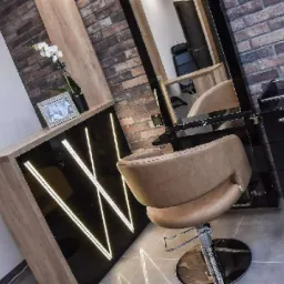 Nowoczesne stanowisko fryzjerskie z beżowym fotelem obrotowym, podświetlaną szafką z dekoracją w romby z ledów i ceglaną ścianą w tle.