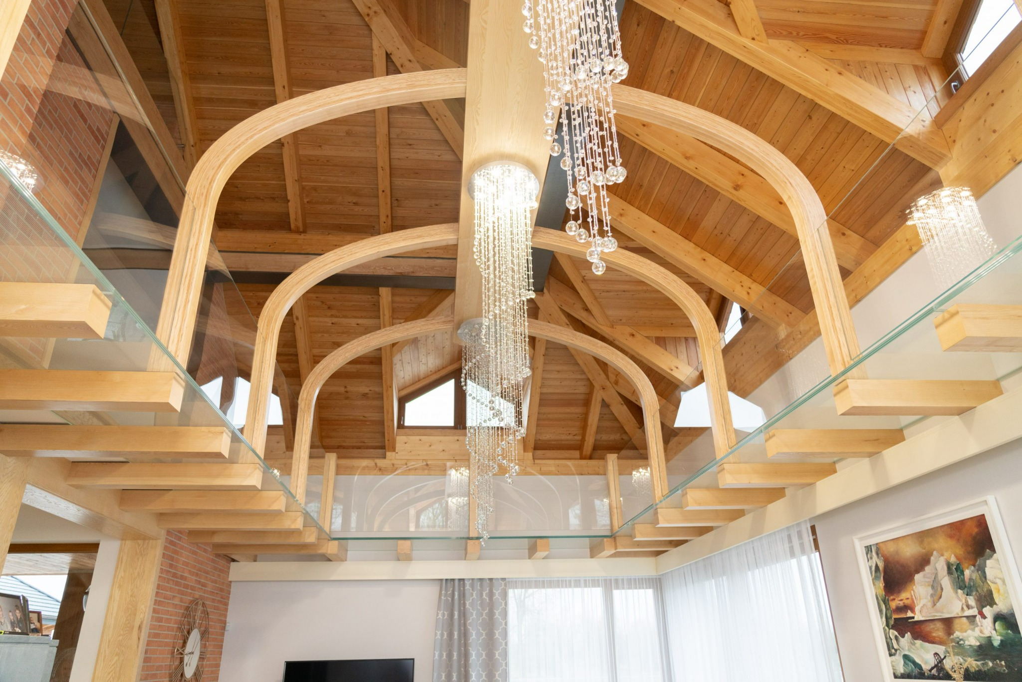 Wysokie wnętrze z drewnianą konstrukcją stropu, szklaną balustradą i kaskadowym kryształowym żyrandolem.