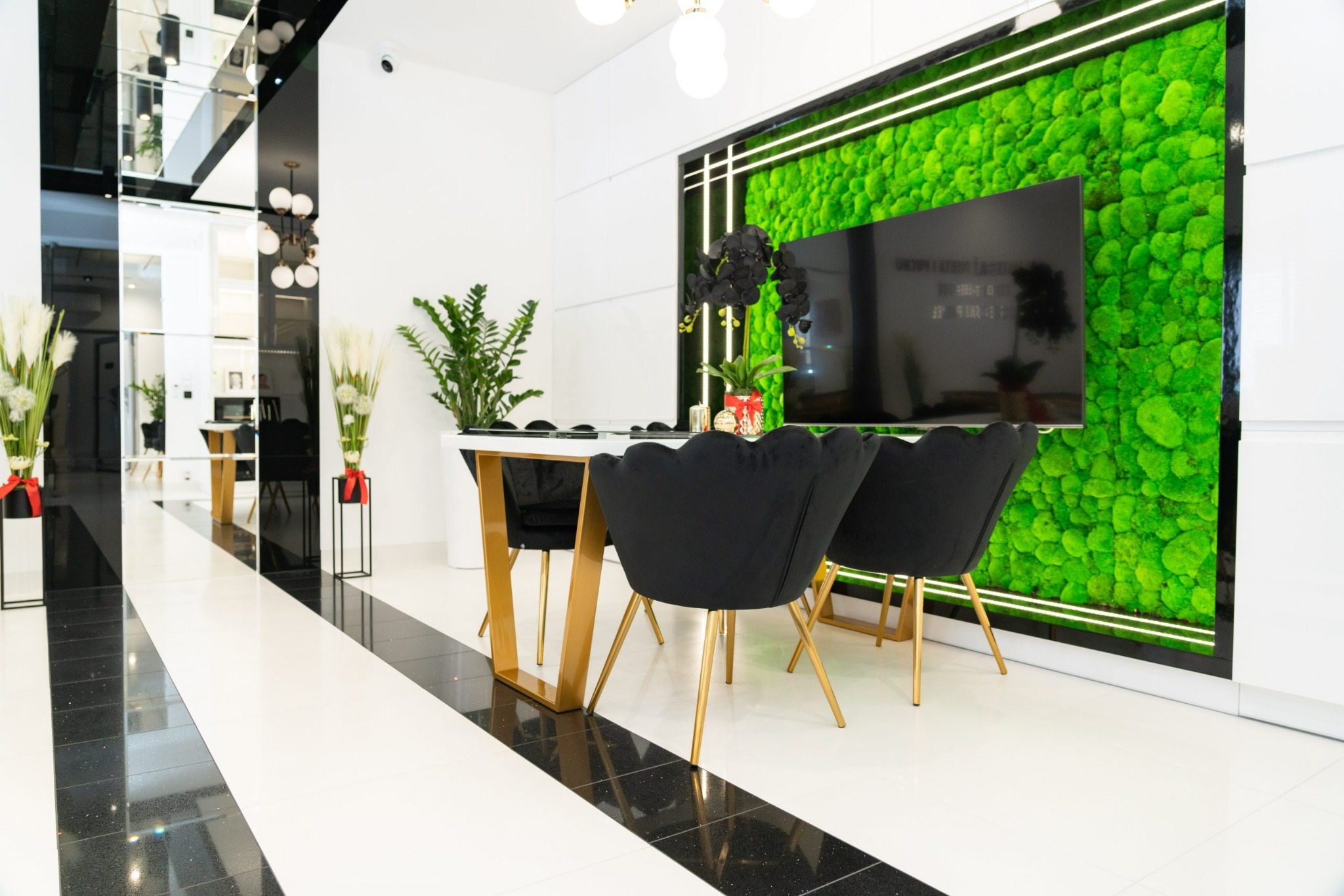 Nowoczesne biuro z białymi ścianami, czarnymi krzesłami i stołem z złotymi nogami, zielona ściana z mchu z podświetleniem LED.